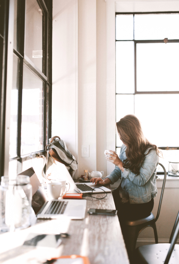 woman working on her computer at a desk while drinking a cup of coffee.